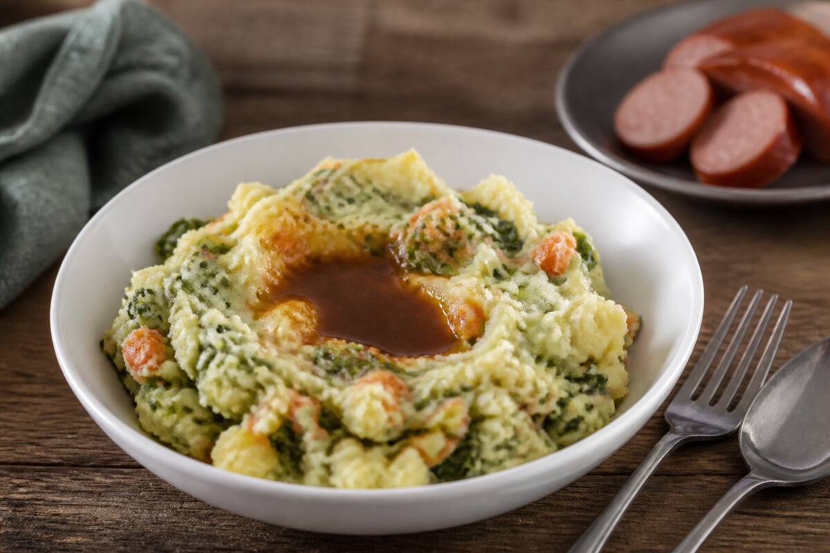 Close-up van een bord stamppot met smeuïge aardappelpuree en groente onder warm licht