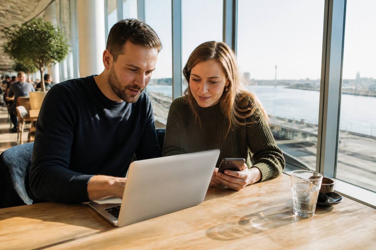 Vakanties vergelijken op laptop en telefoon in een zonnig café